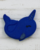 Blue felt narwhal toy on pebbles