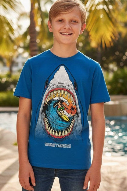 Child wearing a blue t-shirt with a shark graphic design, standing by a pool with palm trees in the background.