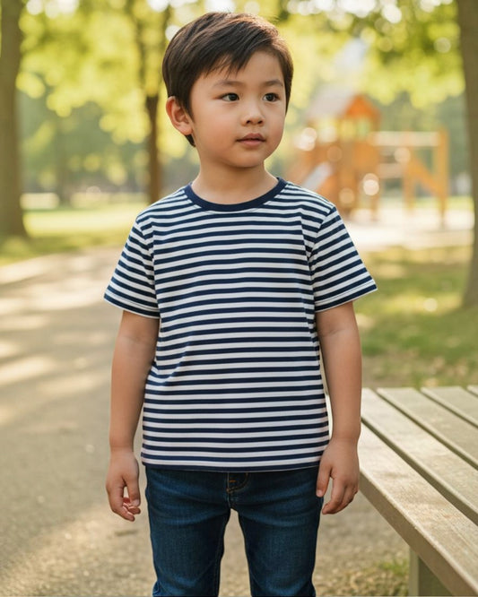 Child wearing a striped shirt standing in a park with trees and a playground in the background