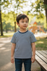 Child wearing a striped shirt standing in a park with trees and a playground in the background