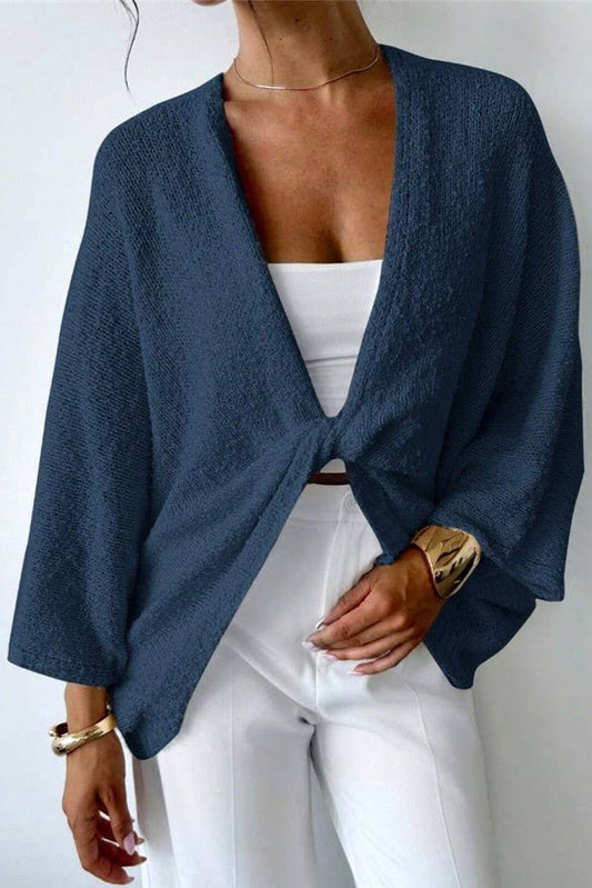 Person wearing a blue cardigan over a white top and pants on a plain background