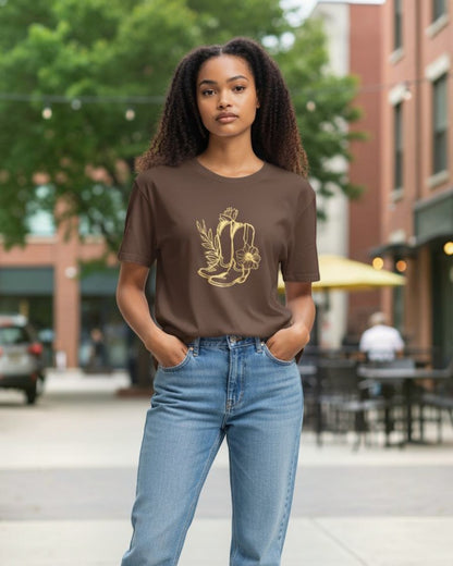 Woman wearing a brown t-shirt with a graphic design and blue jeans standing on a sidewalk.