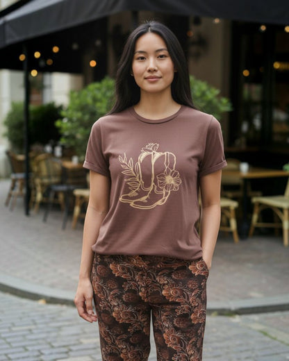 Woman wearing a brown t-shirt with a graphic design and patterned pants standing outdoors.