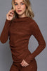 Woman wearing a brown ribbed long-sleeve top against a gray background