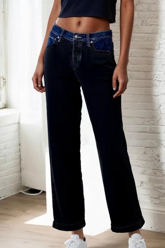 Person wearing dark blue jeans standing indoors with a light-colored wall background