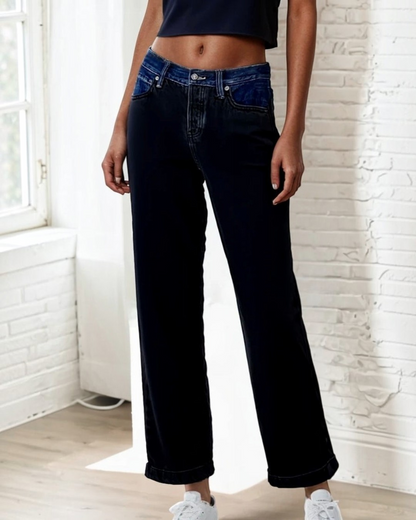 Person wearing dark blue jeans standing indoors with a light-colored wall background