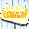 A yellow twinkie bath bomb topped with white frosting and yellow sugar sprinkles on a white tray against a wood background