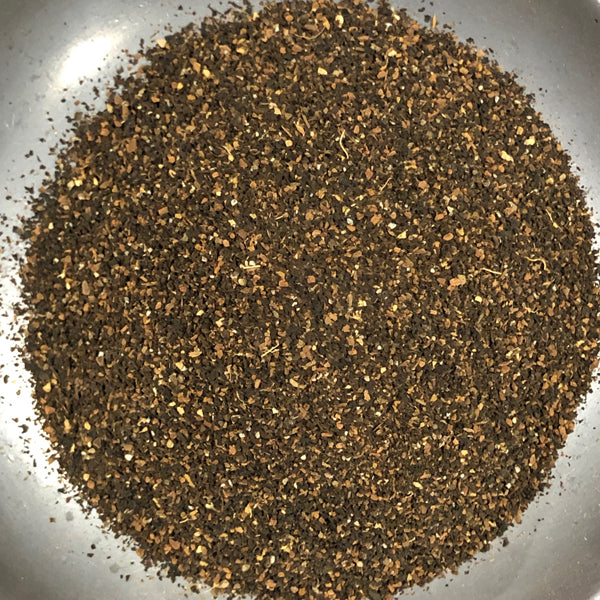 A close-up top-down view of a loose, ground brown herbal tea blend or spice mixture in a silver bowl.