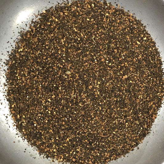 A close-up top-down view of a loose, ground brown herbal tea blend or spice mixture in a silver bowl.