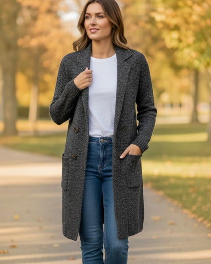Woman wearing a gray coat, white shirt, and blue jeans outdoors.