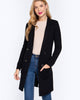 Woman wearing a black coat, beige sweater, and blue jeans on a white background