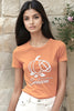 Woman wearing an orange t-shirt with a pumpkin design and text, standing against a stone wall.
