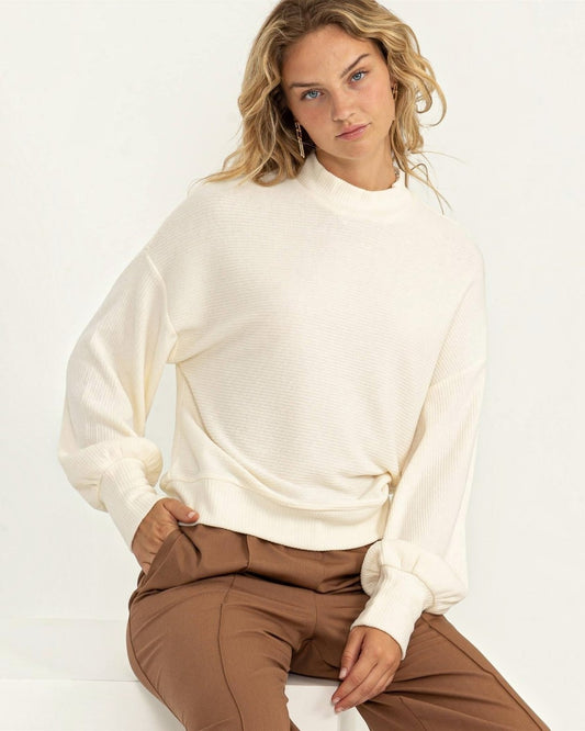 Woman wearing a white sweater and brown pants against a white background