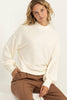 Woman wearing a white sweater and brown pants against a white background