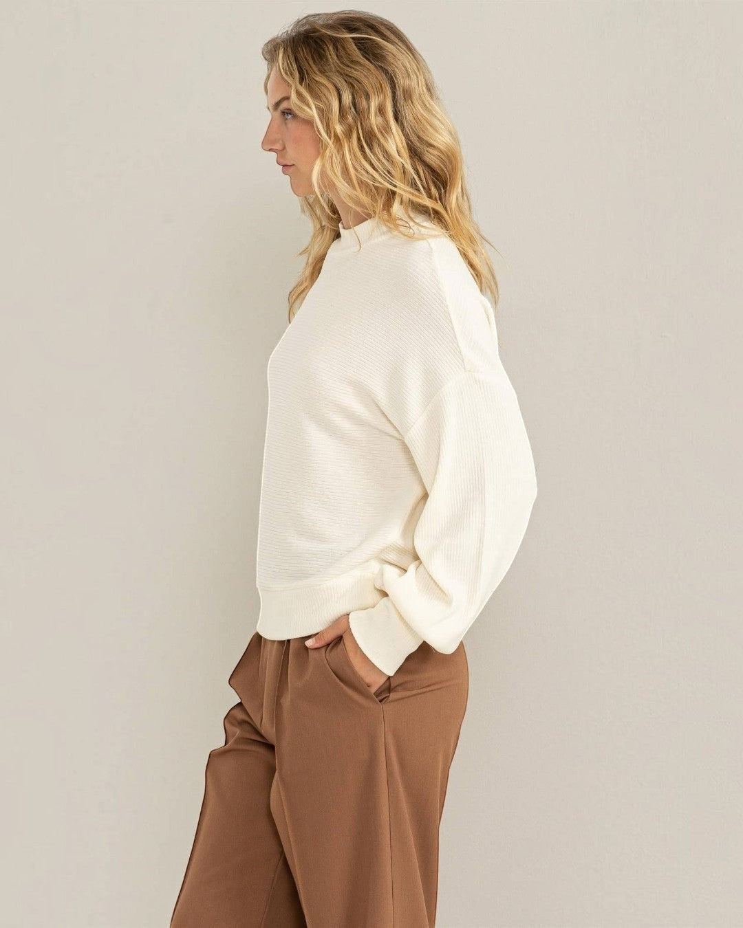 Woman wearing a white blouse and brown pants against a plain background