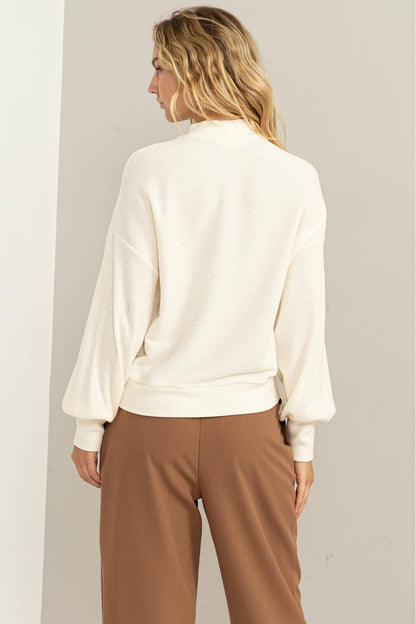 Woman wearing a white blouse and brown pants against a plain background