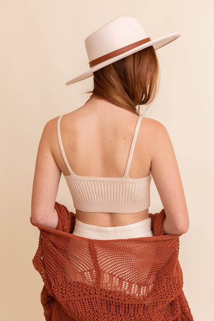 Woman wearing a beige knit top and white pants with a brown woven shawl over her shoulders, on a beige background.
