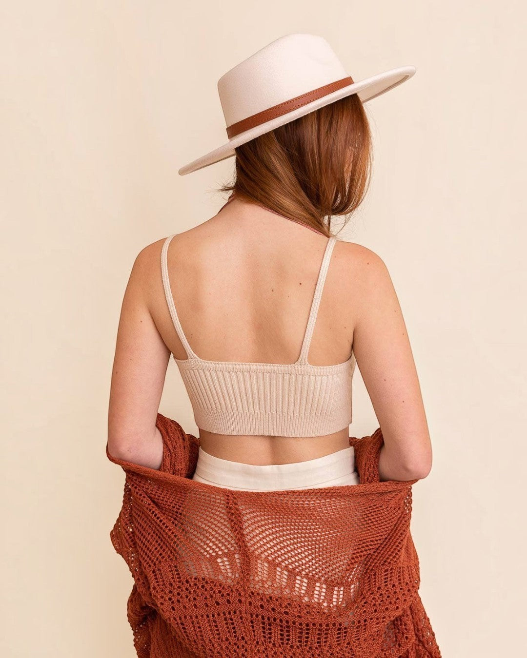 Woman wearing a beige knit top and white pants with a brown woven shawl over her shoulders, on a beige background.