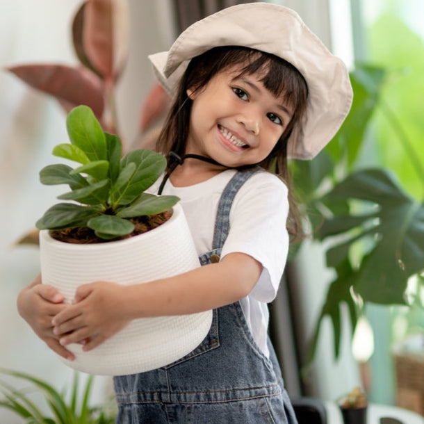 Child holding a potted plant in a room with greenery