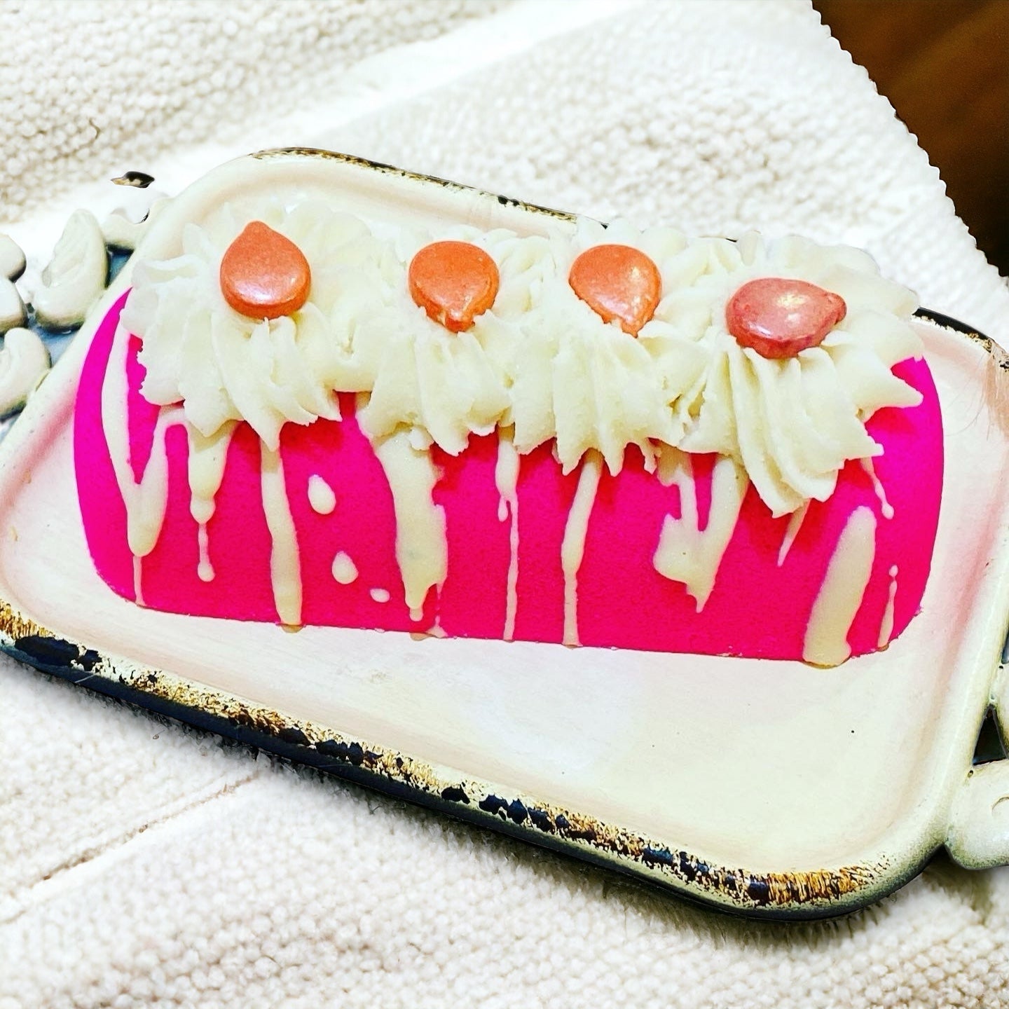 A pink twinkie bath bomb topped with white frosting and sugar sprinkles on a white tray