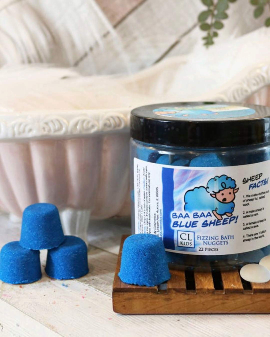 A container of gumdrop shaped blue sheep bath bombs with a tiny 3 bath bomb pyramid to its side