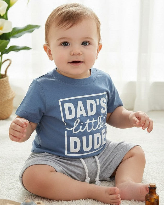 Calla Lily Cosmetics + CL kids blue graphic tee with "DAD'S little DUDE" text and grey shorts with drawstring. Cotton-polyester blend.