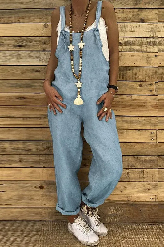 Person wearing light blue denim overalls against a wooden wall.