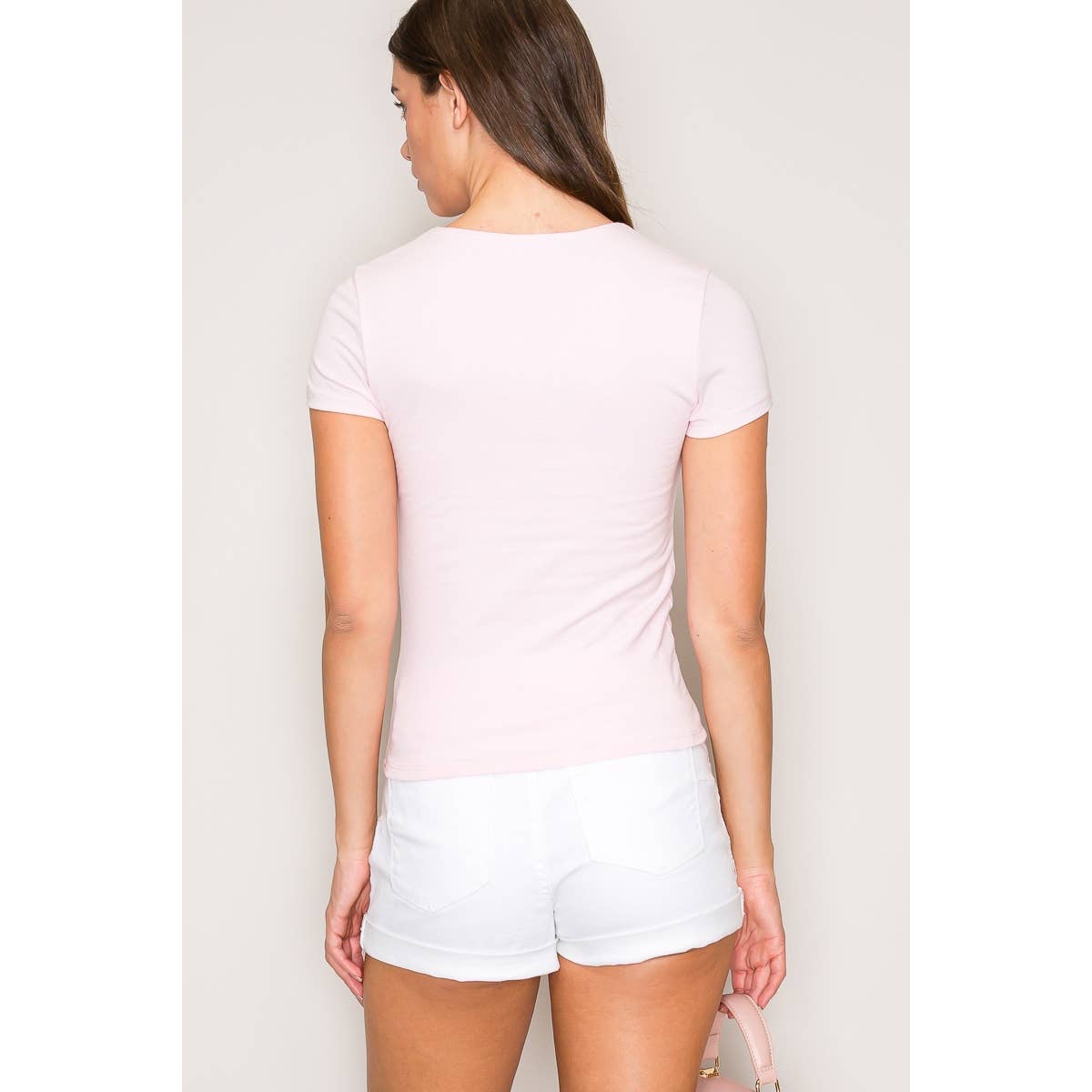 Woman wearing a light pink t-shirt and white shorts against a plain background.