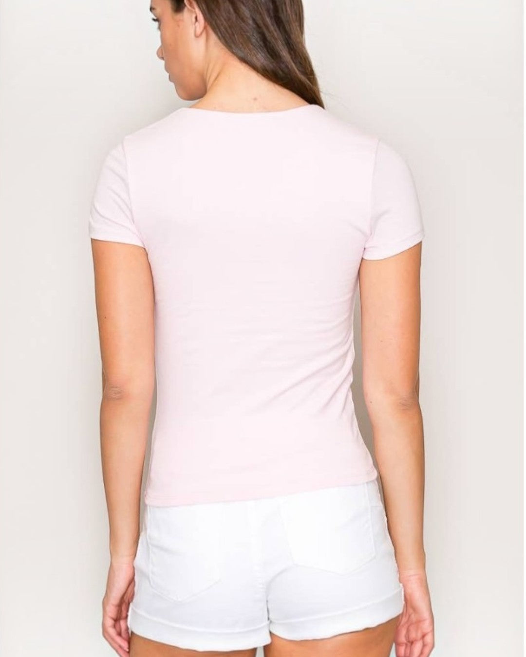 Woman wearing a light pink t-shirt and white shorts against a plain background.