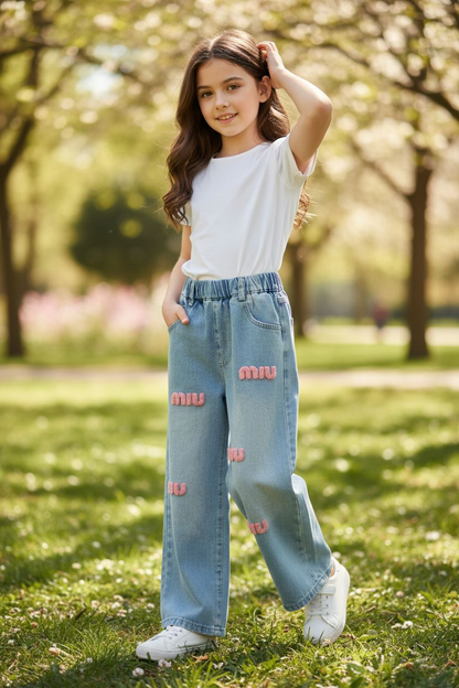 Young girl in a park wearing a white top and blue jeans with pink patterns.