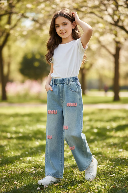 Young girl in a park wearing a white top and blue jeans with pink patterns.