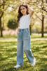 Young girl in a park wearing a white top and blue jeans with pink patterns.
