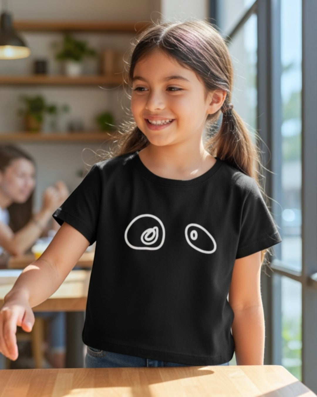Young girl wearing a black t-shirt with white graphics, sitting at a table.
