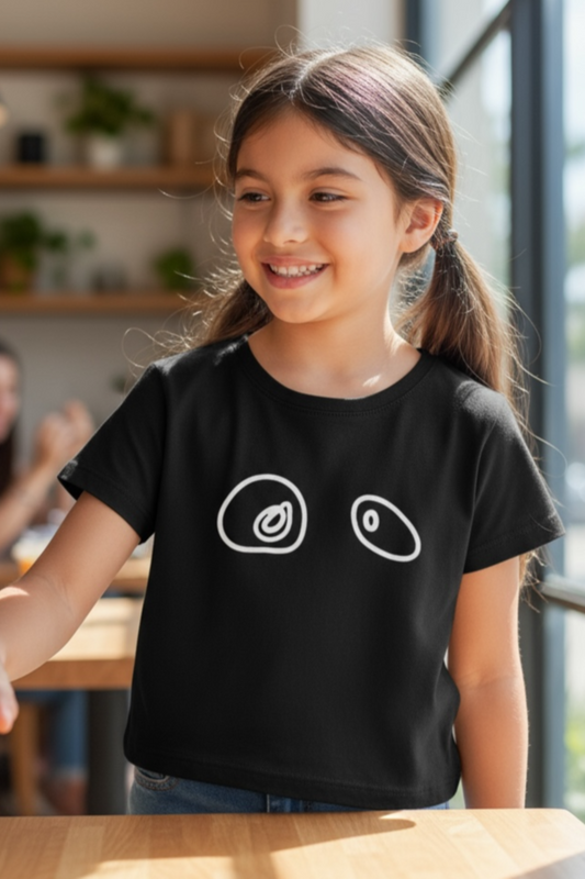 Young girl wearing a black t-shirt with white graphics, sitting at a table.