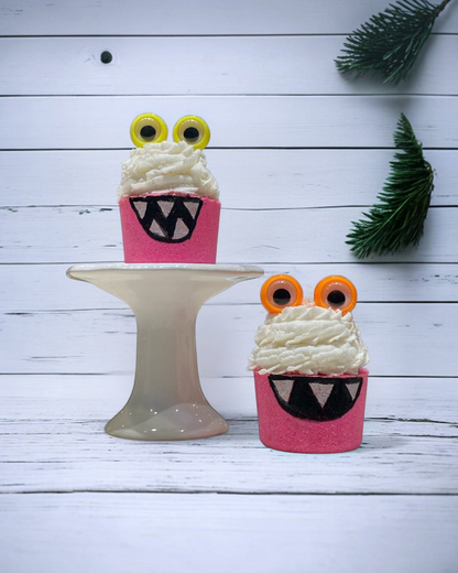 Calla Lily Cosmetics + CL kids pink monster bath bombs with bubble icing and googly eyes on a white cake stand