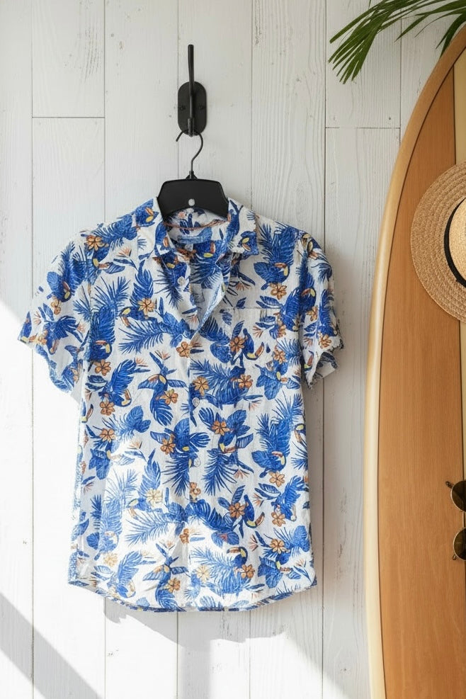 Blue floral shirt on a hanger against a white wooden wall with a surfboard in the background.