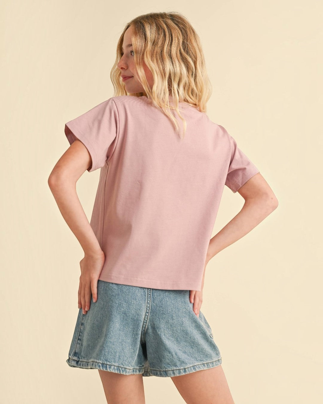 Woman wearing a pink t-shirt and denim shorts on a beige background