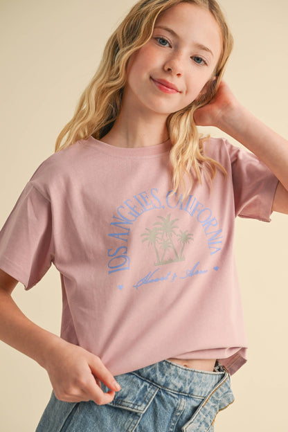 Young girl wearing a pink t-shirt with a palm tree graphic on a beige background