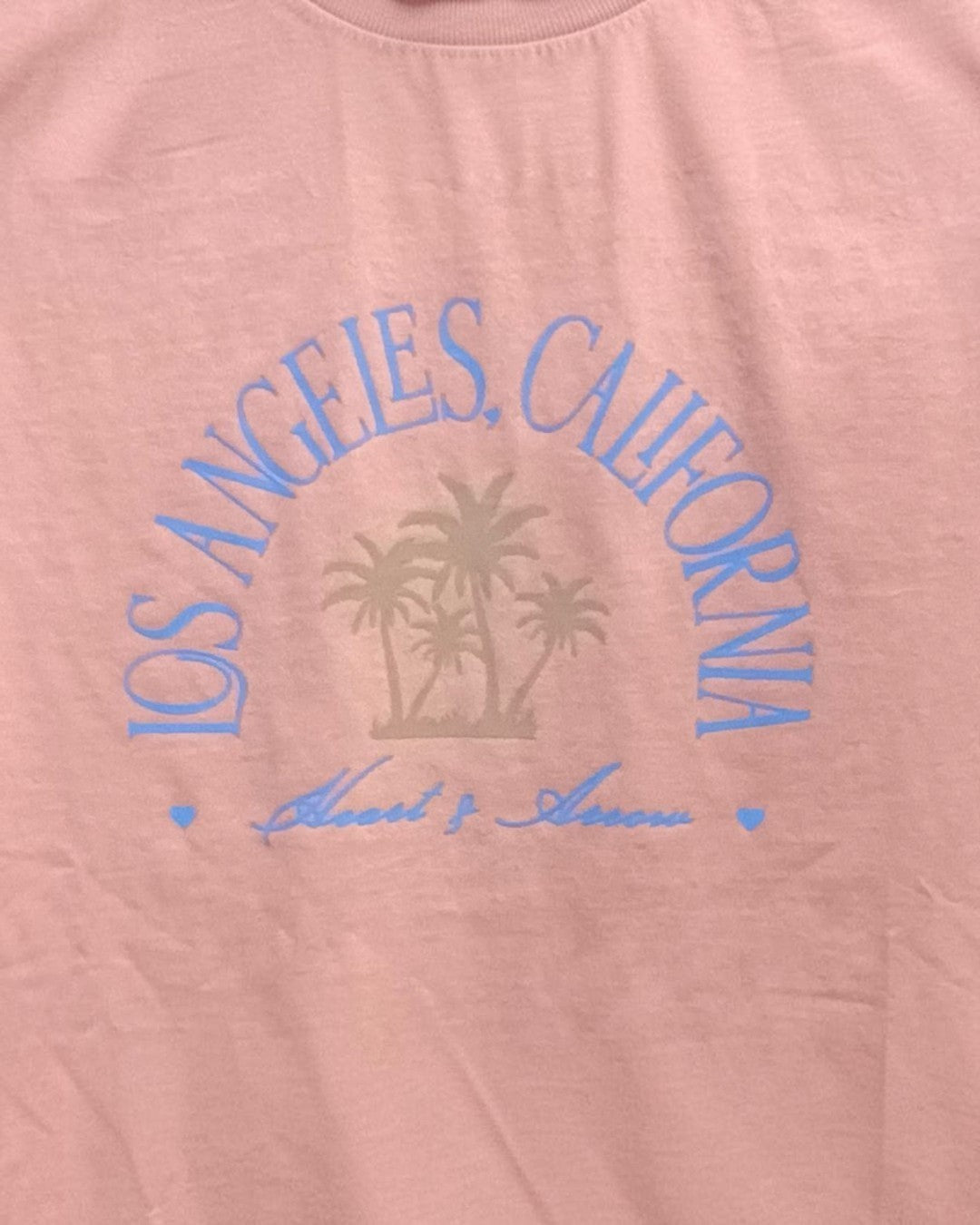 Pink shirt with 'Los Angeles, California' text and palm tree design on a white background