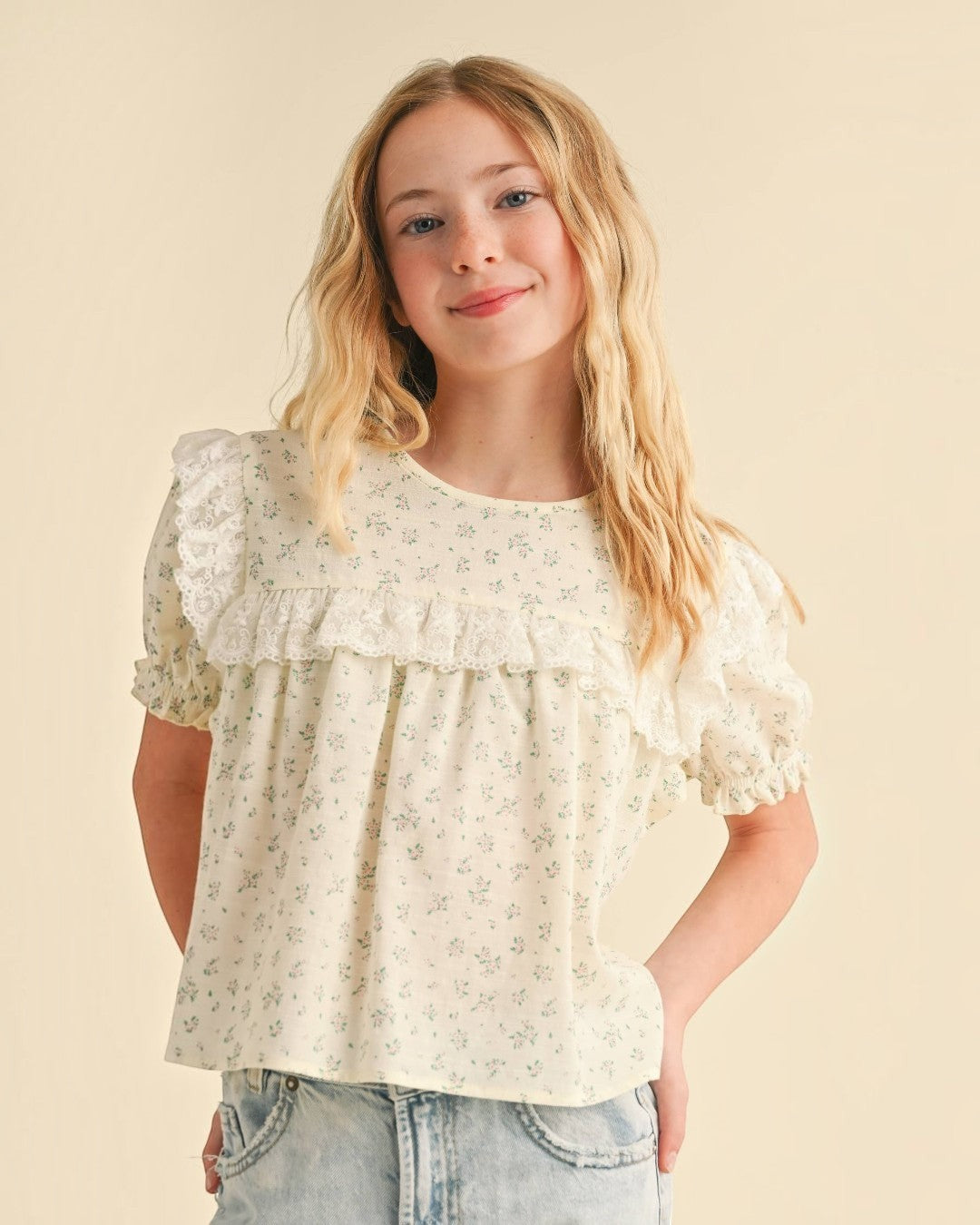 Young girl wearing a floral blouse with puffed sleeves against a beige background
