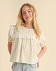 Young girl wearing a floral blouse with puffed sleeves against a beige background
