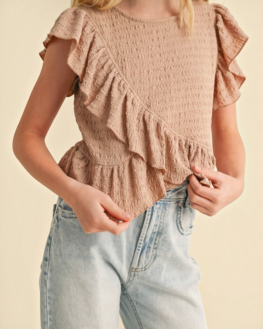 Person wearing a ruffled top and jeans on a beige background