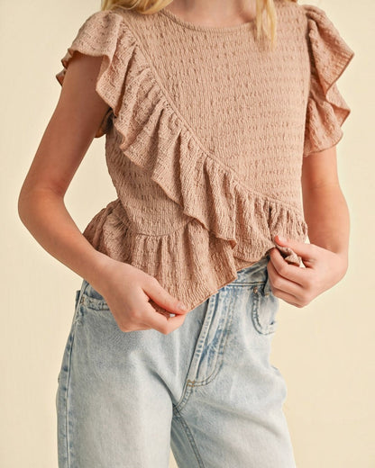 Person wearing a ruffled top and jeans on a beige background