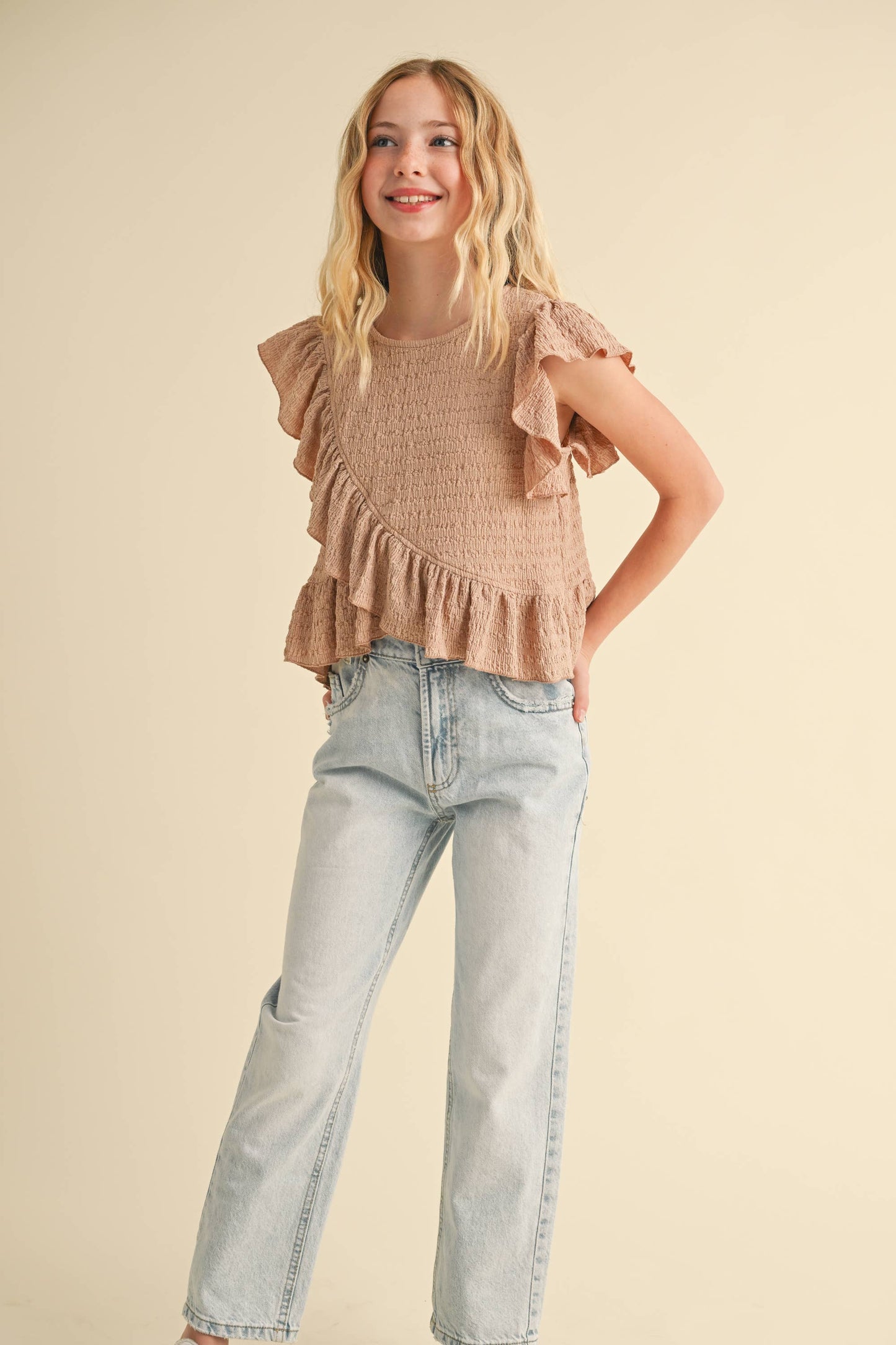 Young girl wearing a ruffled top and jeans on a beige background