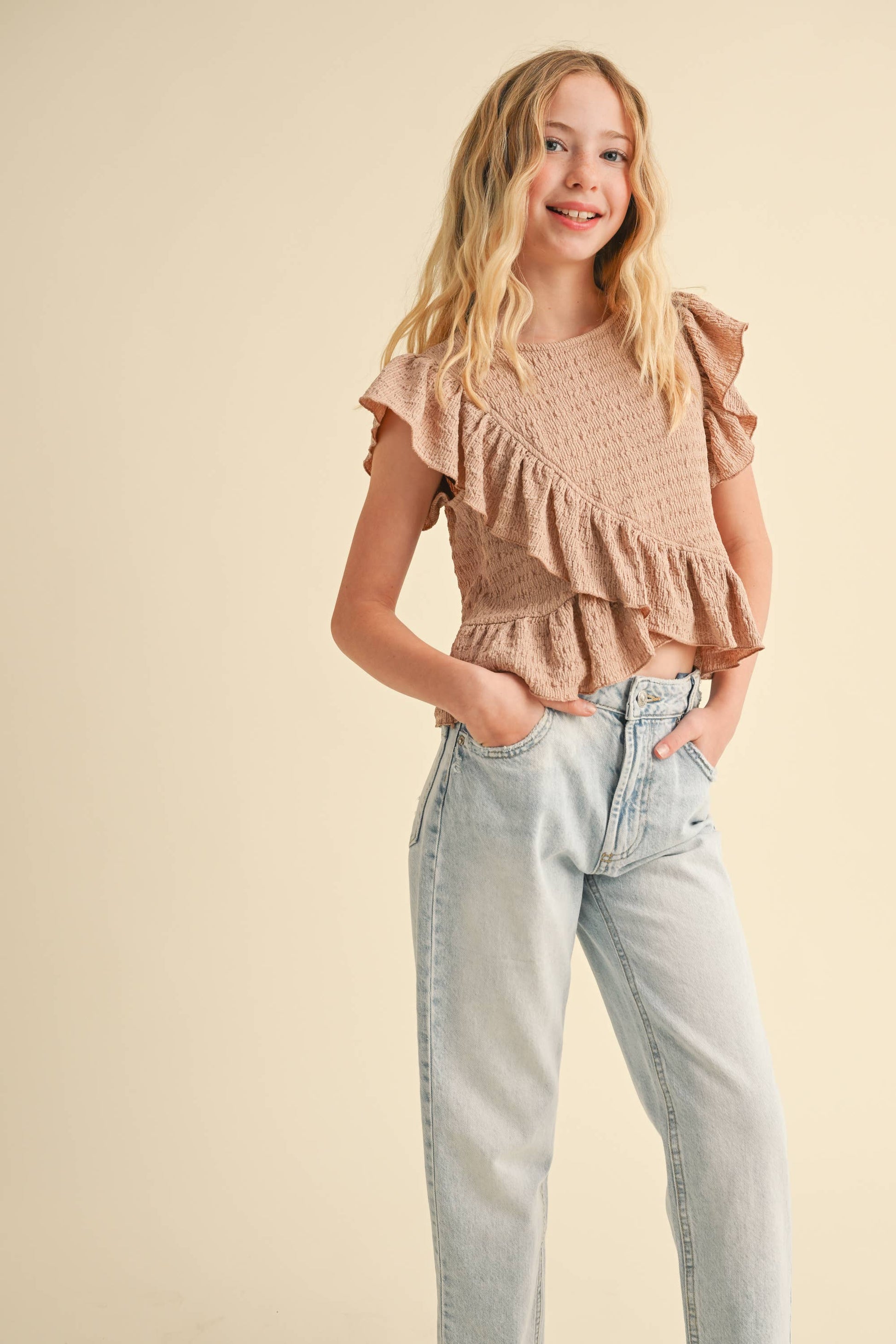 Young girl wearing a ruffled top and jeans on a beige background