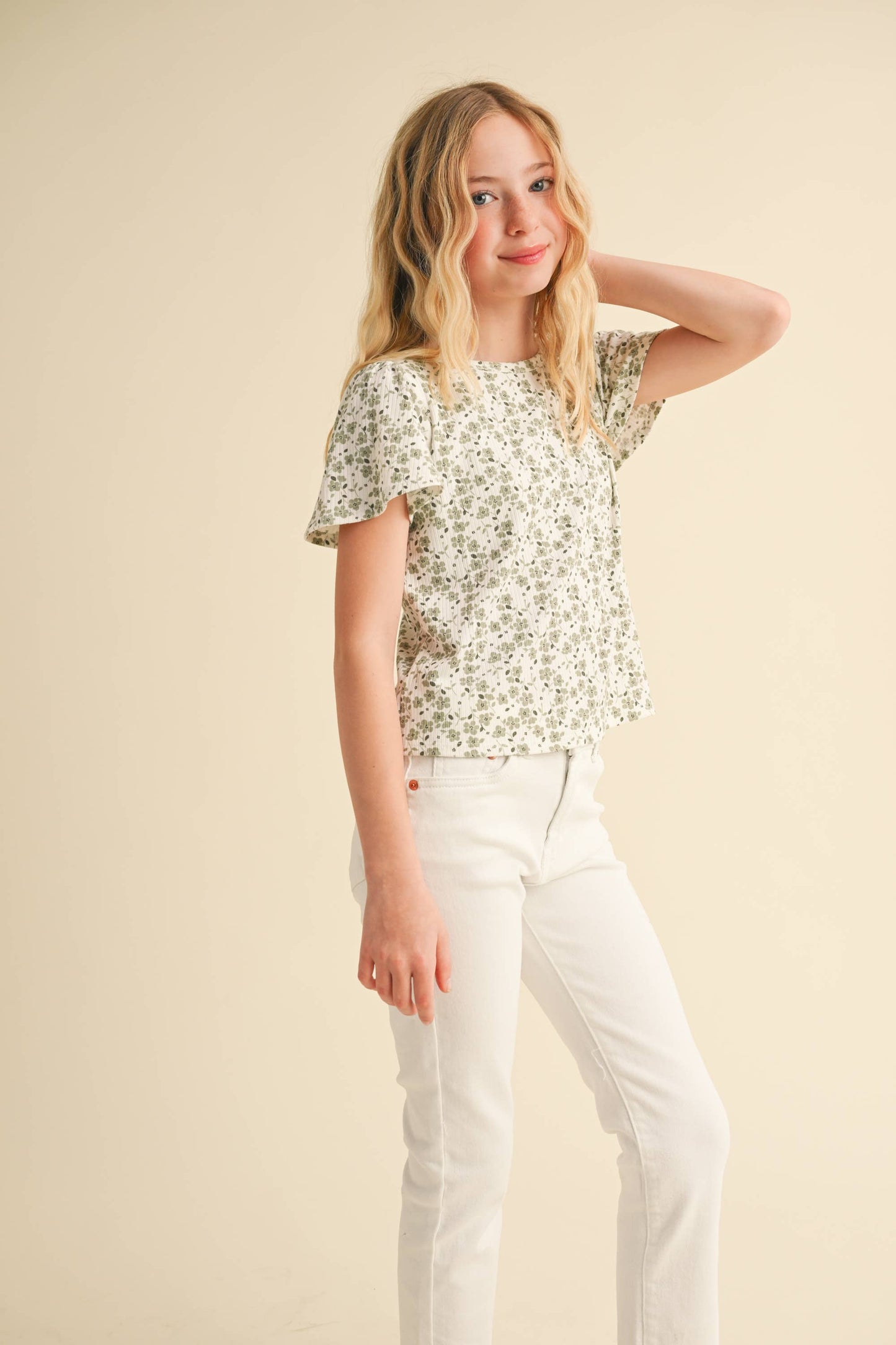 Girl wearing a floral top and white pants against a beige background