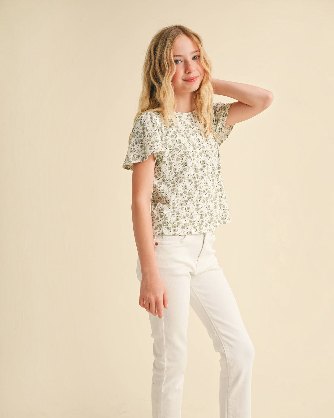 Girl wearing a floral top and white pants against a beige background