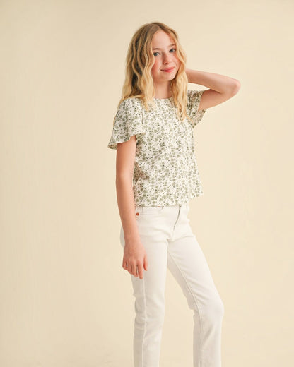 Girl wearing a floral top and white pants against a beige background