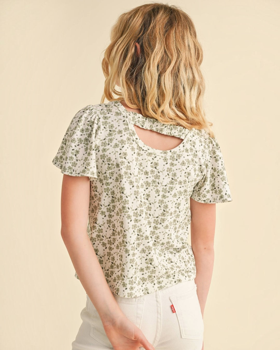 Young girl wearing a floral blouse with a cutout back design on a beige background