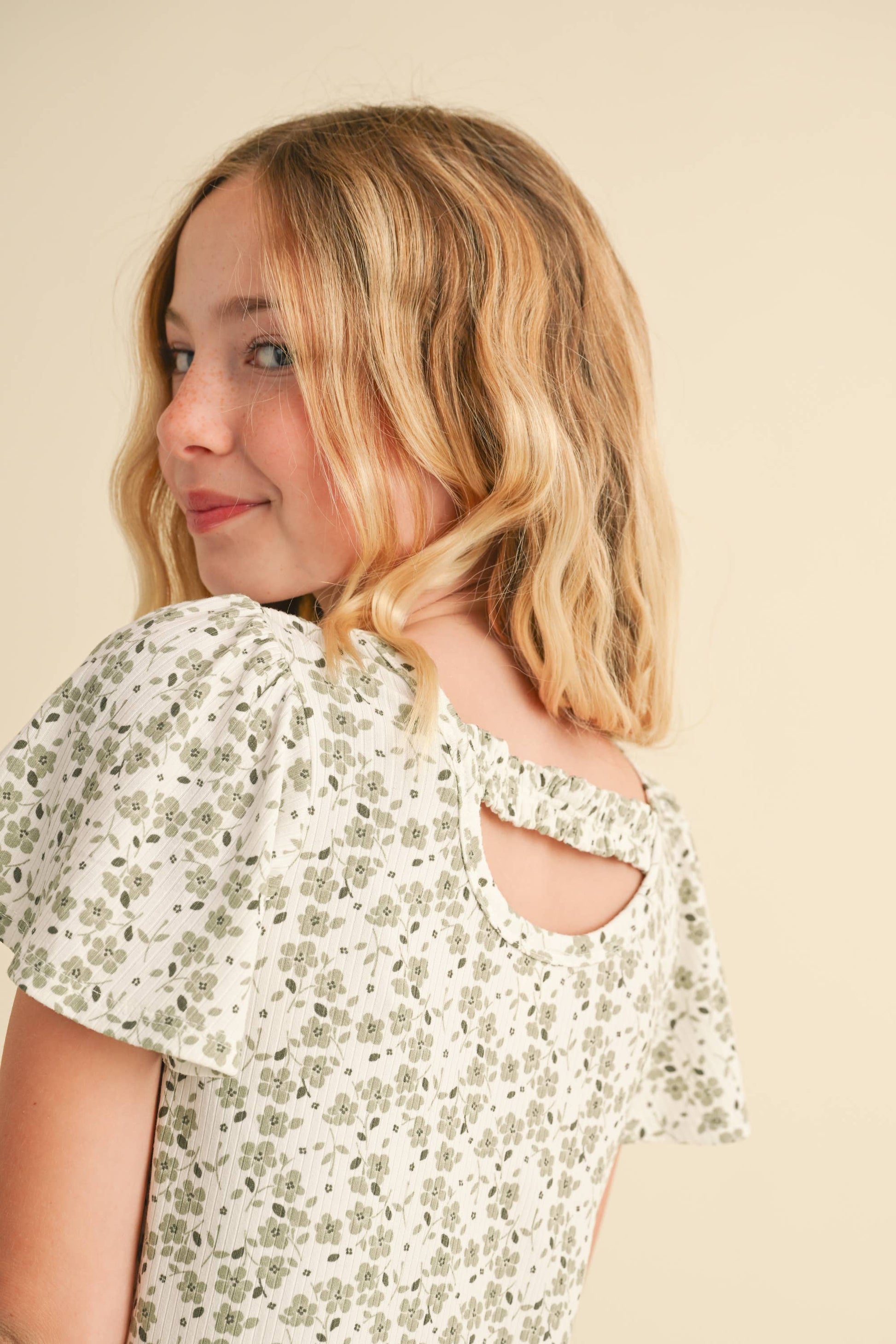 Young girl wearing a floral blouse with cut-out shoulders against a beige background